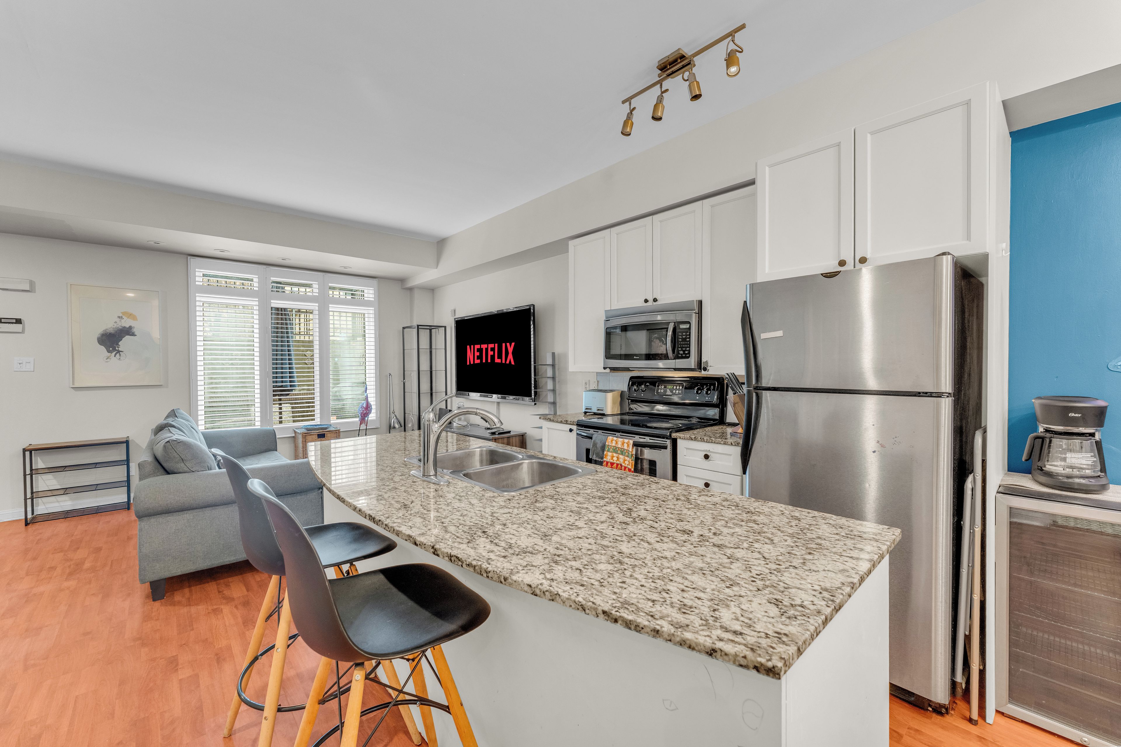 A modern kitchen with a granite countertop, stainless steel appliances, and a flat-screen TV mounted above the microwave.