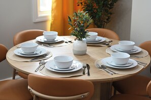 A round dining table with white bowls and plates, accompanied by cutlery, set on a woven placemat. - Hoboken Fun House Walk to PATH Sleeps 7 (Hoboken)
