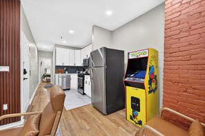 A modern kitchen with stainless steel appliances, a dining area with a wooden table and leather chairs, and a Pac-Man arcade machine. - Hoboken Fun House Walk to PATH Sleeps 7 (Hoboken)