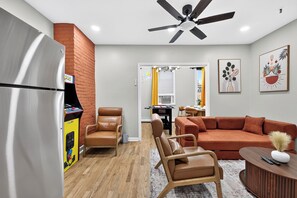 A compact living space with a refrigerator, two chairs, a sofa, a ceiling fan, and artwork on the walls. - Hoboken Fun House Walk to PATH Sleeps 7 (Hoboken)
