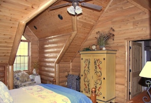A log cabin bedroom with a bed, a wooden cabinet, a ceiling fan, and a window. - Large country home with 4 en suite bedrooms, large living room & chefs kitchen (Amoret)