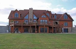 A large, two-story log cabin with a stone chimney, multiple windows, and a balcony. - Large country home with 4 en suite bedrooms, large living room & chefs kitchen (Amoret)