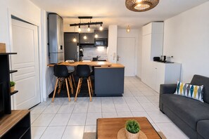 A modern kitchen with a central island, two black chairs, a grey sofa, and a coffee table with a plant.