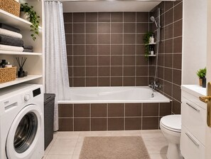 A modern bathroom with a built-in washing machine, a bathtub, and a toilet.