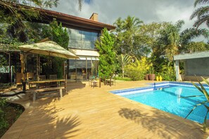 A modern house with a glass conservatory, a wooden deck, and a swimming pool.