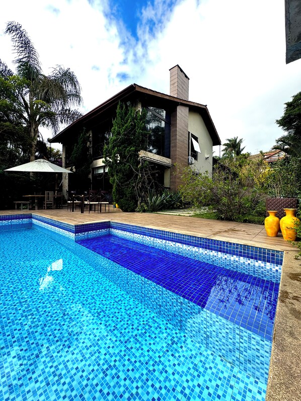 A swimming pool with blue mosaic tiles, surrounded by a patio area with outdoor furniture.