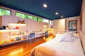 A modern bedroom with a starry ceiling, a large bed, a desk, and shelves with toys.