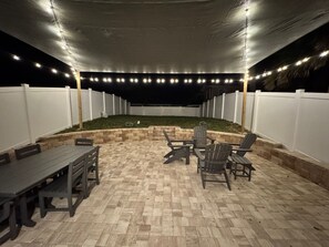 An outdoor patio area with a brick floor, a table and chairs, and string lights. - 3-bedroom townhome STEPS to the beach in gorgeous New Smyrna Beach, pet-friendly (New Smyrna Beach)