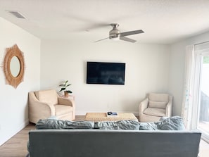 A living room with a ceiling fan, two armchairs, a sofa, a TV, and a decorative mirror. - 3-bedroom townhome STEPS to the beach in gorgeous New Smyrna Beach, pet-friendly (New Smyrna Beach)