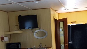Een kamer met een bed, een bureau met stoel, een aan de muur bevestigde televisie en een deur met een waarschuwingsbord.