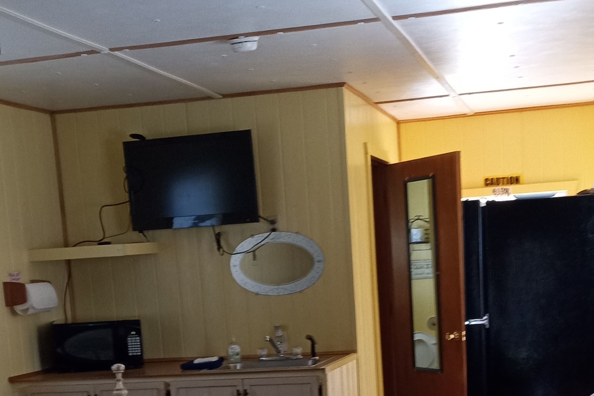 A room with a bed, a desk with a chair, a television mounted on the wall, and a door with a caution sign.