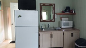 Een functionele keuken met een koelkast, magnetron, spoelbak en houten keukenkastjes.