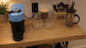 Een koffiehoek met een Nespresso machine, twee glazen bekers, een koffiekan en een bordje met de tekst 'koffie maakt alles beter'.