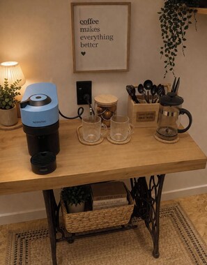 Una estación de café con una máquina Nespresso, dos tazas de vidrio, una cafetera y un letrero que dice 'el café hace todo mejor'.