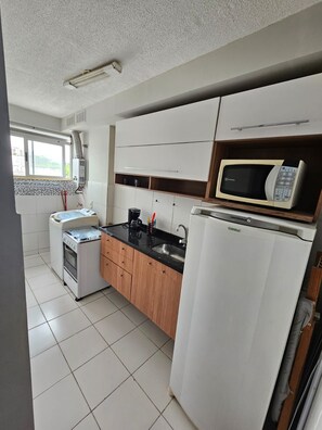 A modern kitchen with white cabinets, a black countertop, a built-in microwave, and a coffee maker. - My beach place: a fully equipped apartment located, close to the Olympic Arenas (Rio de Janeiro)