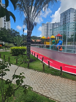 A playground with slides and climbing structures, surrounded by a red pathway and greenery. - My beach place: a fully equipped apartment located, close to the Olympic Arenas (Rio de Janeiro)