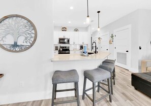 Una cocina moderna con armarios blancos, una isla central con taburetes y luminarias colgantes.