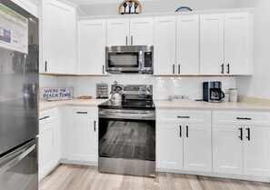 A modern kitchen with white cabinets, stainless steel appliances, and a sign indicating a beach theme. - Lux Beach House - 2-Min Beach - Hot Tub - Dogs OK (Panama City Beach)