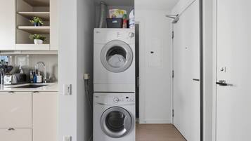 A compact laundry room with stacked washing machines, a small kitchen area with a toaster, and a door leading to another room.