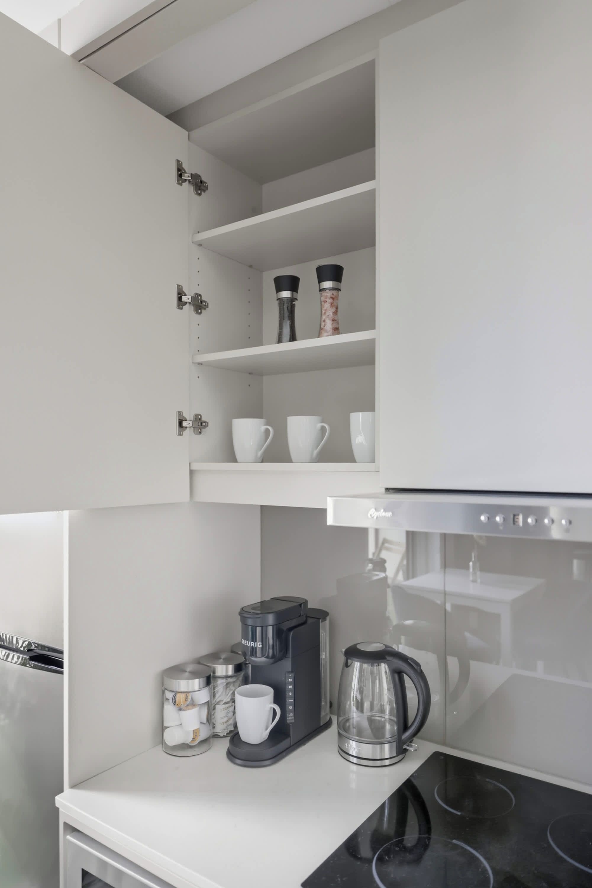 A kitchen with white cabinetry, a coffee maker, a kettle, and a coffee grinder on the countertop.