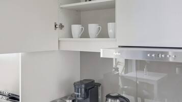 A kitchen with white cabinetry, a coffee maker, a kettle, and a coffee grinder on the countertop.