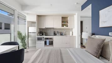 A modern hotel room with a kitchenette, a bed with a large window, and a view of the city.
