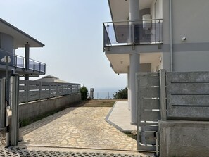 Ein modernes Gebäude mit einem pflasterbelagten Eingangsbereich, einem verschlossenen Bereich und Blick aufs Meer.