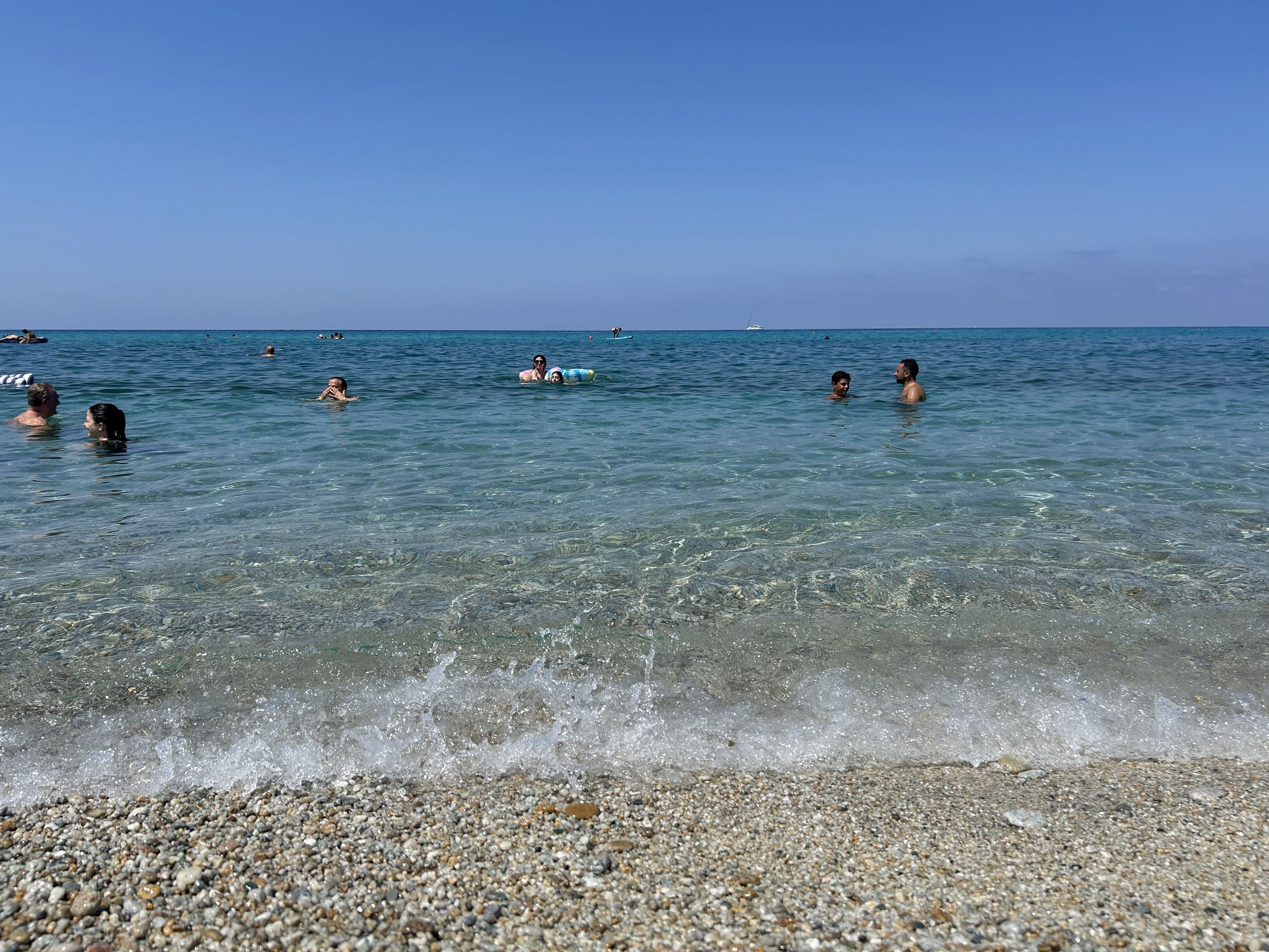 A beach with clear water and pebbles.