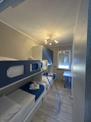Ein kleines Zimmer mit Etagenbetten, einem kleinen Schreibtisch und einem Fenster mit Jalousien.
