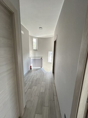 Ein Flur mit Holzboden, einem Fenster und einer T ür links.