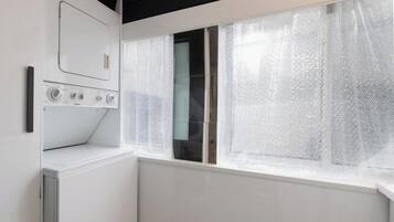 Ein Waschraum mit Waschmaschine, Trockner und einem Fenster mit durchsichtigen Vorhängen.