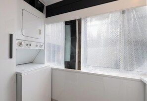 A laundry room with a washing machine, a dryer, and a window with sheer curtains.