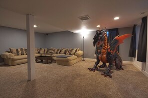 A living room with a beige carpet, a sofa with patterned cushions, and a decorative dragon statue. - Spacious 4BR Home - Sleeps 8 - Home Theater, Fenced Yard & BBQ (Thornton)