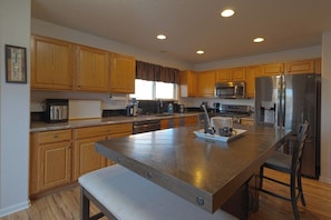 A modern kitchen with wooden cabinets, stainless steel appliances, and a central island with seating. - Spacious 4BR Home - Sleeps 8 - Home Theater, Fenced Yard & BBQ (Thornton)