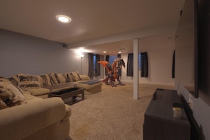 A living room with a sofa, a coffee table, a television, and a decorative dragon statue. - Spacious 4BR Home - Sleeps 8 - Home Theater, Fenced Yard & BBQ (Thornton)