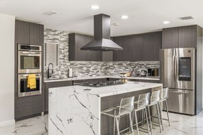 A modern kitchen with a central island, stainless steel appliances, and a tiled backsplash. - The Marilyn: Gorgeous 4-bedroom House with AC in Sunny Palm Springs (Palm Springs)