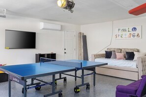 A room with a ping pong table, a sofa, a television, and a wall with a children's artwork. - The Marilyn: Gorgeous 4-bedroom House with AC in Sunny Palm Springs (Palm Springs)