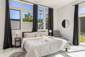 A modern bedroom with a large bed, a round mirror, and a view of greenery outside. - The Marilyn: Gorgeous 4-bedroom House with AC in Sunny Palm Springs (Palm Springs)