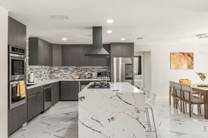 A modern kitchen with a central island, built-in appliances, and a dining area with a chandelier. - The Marilyn: Gorgeous 4-bedroom House with AC in Sunny Palm Springs (Palm Springs)