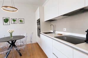 Une cuisine moderne avec des armoires blanches, un comptoir noir et un évier en acier inoxydable. Trois tableaux encadrés représentant des cactus ornent le mur, et un vase rempli de fleurs est posé sur la table à manger.