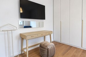 Une pièce comprenant un bureau en bois, un miroir, un téléviseur fixé au mur et une armoire.