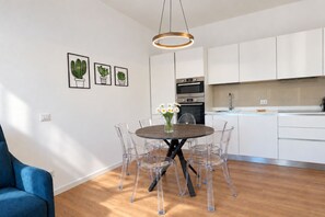 A modern kitchen with white cabinets, a round dining table with clear chairs, and a hanging light fixture. - Elegantis Trastevere Family Apartment with Terrace (Roma)
