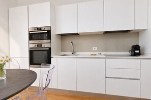 A modern kitchen with white cabinets, stainless steel appliances, a sink, and a coffee maker. - Elegantis Trastevere Family Apartment with Terrace (Roma)
