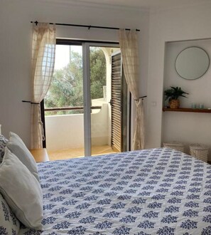 A bedroom with a bed, curtains, a sliding glass door to a balcony, and a small shelf with a plant. - Home - Family Vacations (Albufeira)