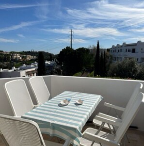 A balcony with a table and chairs, overlooking a residential area with houses and trees. - Home - Family Vacations (Albufeira)