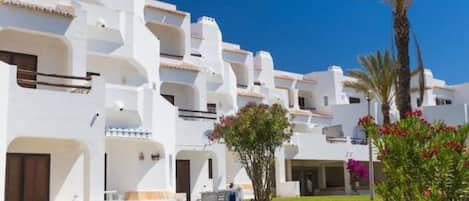 A row of white buildings with balconies, a clear blue sky, and a palm tree.