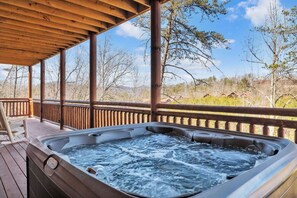 A hot tub on a wooden deck with a view of trees and hills. - 8BR • 25 Beds • Indoor Pool • Tiki Bar • Hot Tub (Sevierville)