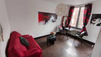 A modern living room with a red sofa, a dining table with chairs, and a large abstract painting on the wall.
