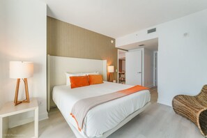 A modern hotel room with a large bed, two bedside lamps, a wicker chair, and a visible bathroom in the background. - 30th Floor Two Condo Vacation Package in Hollywood (Hollywood)