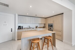 A modern kitchen with a central island, wooden stools, and built-in appliances. - Unbeatable Luxury Penthouse Combo with Ocean Views (Hollywood)